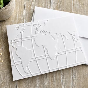 May include: A white folded greeting card featuring a raised embossed world map design with longitudinal and latitudinal grid lines. The card is accompanied by a matching plain white envelope, both made of heavy cardstock with a clean finish.