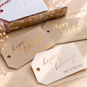 May include: A collection of rectangular gift tags with angled corners, featuring the text Happy Holidays and From: The Perry Family in metallic gold, copper, and rose gold foil. The tags are made of kraft paper and cream cardstock with holes.
