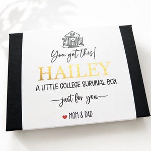 Op de afbeelding: Een rechthoekige zwarte geschenkdoos met een witte papieren wikkel met een zwarte lijntekening van een schoolgebouw, de tekst "You got this! HAILEY A LITTLE COLLEGE SURVIVAL BOX just for you" in goud en zwart, en een rood hartje.