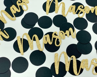 May include: Gold glitter confetti with the name "Mason" written in cursive on each piece. The confetti is scattered on a white background with black circles.