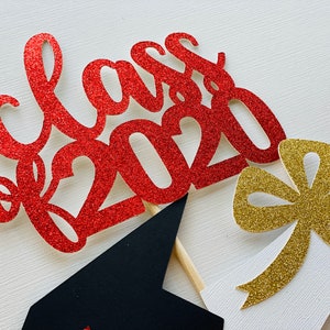 May include: Red glitter "Class of 2020" cake topper with a black graduation cap and a gold glitter bow. The graduation-themed decorations are on wooden sticks, perfect for a celebratory cake.