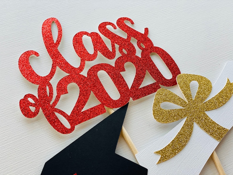 May include: Red glitter "Class of 2020" cake topper with a black graduation cap and a gold glitter bow. The graduation-themed decorations are on wooden sticks, perfect for a celebratory cake.