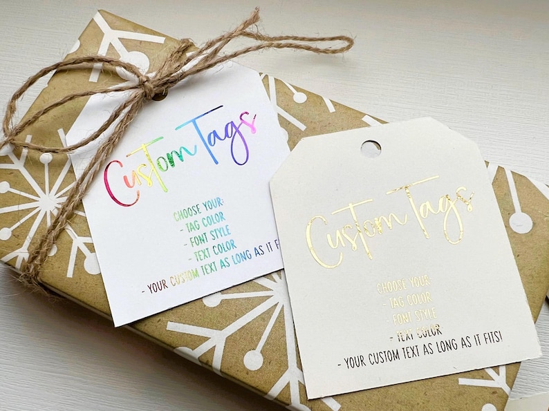 K&ouml;nnte beinhalten: Zwei Geschenkanh&auml;nger mit dem aufgedruckten Text "Custom Tags". Der obere Anh&auml;nger hat regenbogenfarbene Schrift und der untere Anh&auml;nger hat goldene Schrift. Beide Anh&auml;nger enthalten Anweisungen zur individuellen Gestaltung mit Text, Anh&auml;ngerfarbe, Schriftstil und Textfarbe.