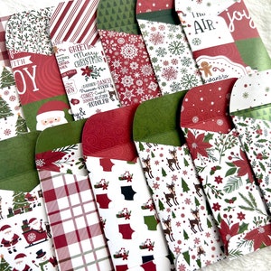 May include: A collection of Christmas-themed envelopes with various patterns, including snowflakes, Santa Claus, reindeer, and plaid. The envelopes feature red, green, and white colors, with some displaying text like "Joy" and "Merry Christmas."