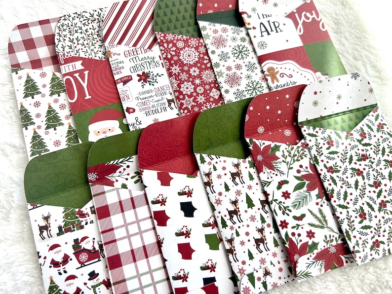 May include: A collection of Christmas-themed envelopes with various patterns, including snowflakes, Santa Claus, reindeer, and plaid. The envelopes feature red, green, and white colors, with some displaying text like "Joy" and "Merry Christmas."