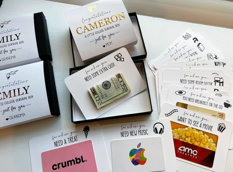 Op de afbeelding: Een verzameling witte geschenkdozen en kaarten voor een college survivalpakket. De dozen bevatten zwarte en gouden tekst met namen zoals Cameron en Emily. De kaarten tonen zinnen zoals Need Some Extra Cash met een biljet van twintig dollar.