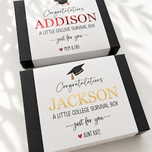 Op de afbeelding: Twee rechthoekige zwarte geschenkdozen met witte hoezen. De bovenste hoes leest Congratulations ADDISON A LITTLE COLLEGE SURVIVAL BOX just for you MOM & DAD. De onderste hoes leest Congratulations JACKSON A LITTLE COLLEGE SURVIVAL BOX just for you AUNT KATE.