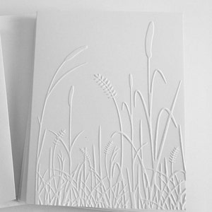 Op de afbeelding: Een witte rechthoekige wenskaart met een verhoogd reli&euml;fontwerp van diverse wilde grassen en lisdodden. De textuur wordt gecre&euml;erd door de in reli&euml;f aangebrachte lijnen op het papieroppervlak, die een veld met hoge planten in wit weergeven.