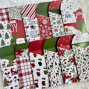 May include: A collection of Christmas-themed envelopes with various patterns, including trees, snowflakes, and Santa Claus. Some envelopes feature text like "Joy" and "Merry Christmas." The envelopes are red, green, and white.