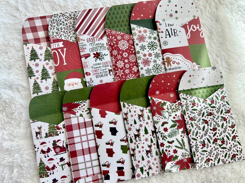 May include: A collection of Christmas-themed envelopes with various patterns, including trees, snowflakes, and Santa Claus. Some envelopes feature text like "Joy" and "Merry Christmas." The envelopes are red, green, and white.