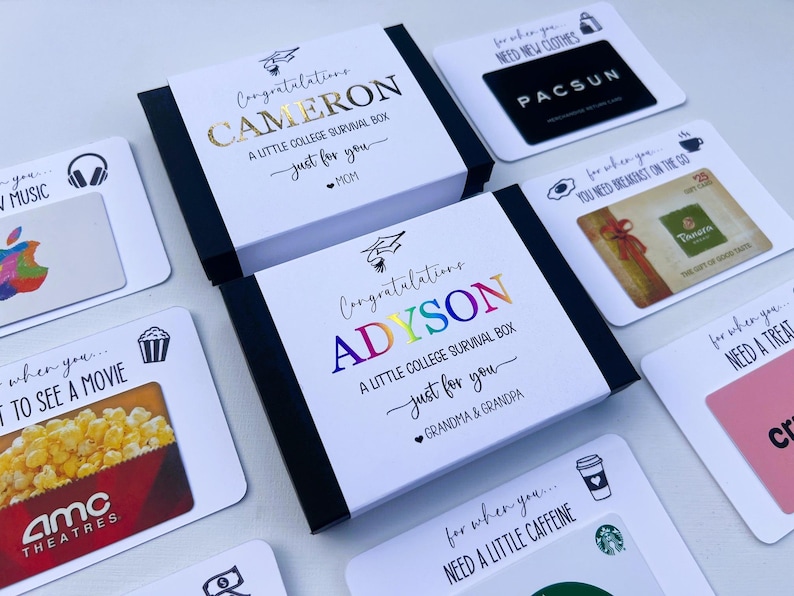 Op de afbeelding: Twee zwarte geschenkdozen met witte hoezen met de tekst Congratulations CAMERON A LITTLE COLLEGE SURVIVAL BOX en Congratulations ADYSON A LITTLE COLLEGE SURVIVAL BOX omringd door diverse cadeaubonnen met labels zoals NEED NEW CLOTHES.