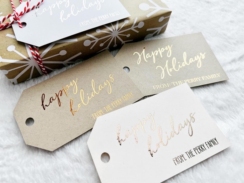 May include: A collection of rectangular gift tags with angled corners and a circular hole. The tags feature the metallic foil text Happy Holidays and FROM: THE PERRY FAMILY in various colors including gold, rose gold, and white on kraft or white cardstock.