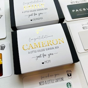 May include: Two black boxes with white lids, labeled "EMILY" and "CAMERON" in gold lettering, with the text "A LITTLE COLLEGE SURVIVAL BOX." Gift cards and other items surround the boxes, including a Pacsun gift card and a Starbucks gift card.