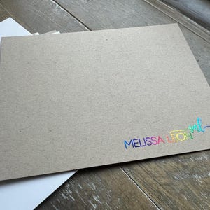 May include: A rectangular piece of tan kraft paper cardstock featuring the text MELISSA LEON in a vibrant, iridescent rainbow foil finish. The text is positioned in the bottom right corner, accompanied by a stylized script monogram of the letters ml.