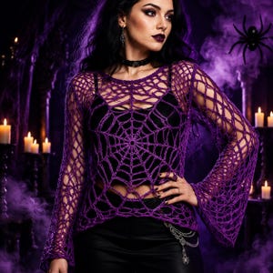May include: A long-sleeved purple crochet top featuring a prominent spiderweb pattern across the front, worn over a black camisole. The garment has a loose, open-knit construction with flared sleeves and a round neckline, showcasing intricate yarn work.