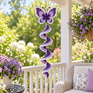 May include: A hanging crochet decoration featuring a purple and white butterfly at the top, connected to a long, spiraling, multi-layered crochet tail in shades of purple and white, accented with small white beads along the central vertical strand.