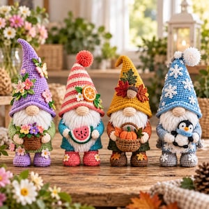 Op de afbeelding: Vier gehaakte kabouters staan op een rij. De eerste is paars met bloemen, de tweede heeft rood-witte strepen met fruit, de derde is geel met herfstbladeren en een pompoen, de vierde is blauw met witte sneeuwvlokken en een kleine pinguïn.