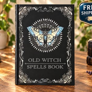 May include: A black hardcover book with the text OLD WITCH SPELLS BOOK printed in white. The cover features a central illustration of a butterfly with light blue and cream wings, surrounded by a decorative white filigree border on all four sides.