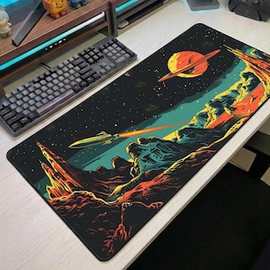 Può includere: Un tappetino da scrivania rettangolare con un'illustrazione a tema spaziale su sfondo nero, un grande pianeta arancione con anelli, un razzo che emette una lunga scia arancione e un terreno roccioso e frastagliato nei toni dell'arancione, giallo e ottanio.