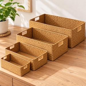 May include: A set of four rectangular storage baskets in graduated sizes, each featuring a woven tan texture and integrated side handles. The baskets are arranged in a cascading formation, showcasing a consistent light brown color and open top design.