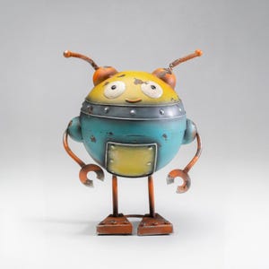 May include: A round metal robot figurine featuring a yellow head with white eyes, a teal torso with a yellow square panel, and orange limbs. The robot has two antennae with coiled springs and claw-shaped hands, finished with a distressed texture.