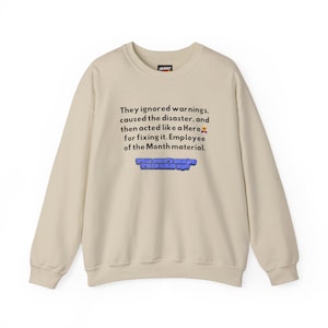 May include: A beige crewneck sweatshirt featuring black text that reads: They ignored warnings, caused the disaster, and then acted like a Hero for fixing it. Employee of the Month material. Below is blue text reading: YOU CAN'T MAKE THIS SHIT UP.