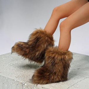 May include: A pair of ankle-height boots covered in long, shaggy faux fur in shades of brown, tan, and black. The boots feature a rounded toe design and a thick, plush texture that extends from the base to the top opening of the footwear.
