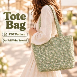 May include: A green tote bag with a white daisy floral pattern, featuring two shoulder straps and an exterior pocket. The image includes the text "Tote Bag", "PDF Pattern", and "Full Video Tutorial" in dark green lettering on the left side.