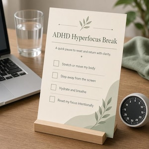 May include: A rectangular card in a light wooden stand featuring the text ADHD Hyperfocus Break, a sub-heading, and a checklist with four items: Stretch or move my body, Step away from the screen, Hydrate and breathe, and Reset my focus intentionally.
