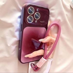 May include: A deep burgundy smartphone case with a glossy finish and a camera lens protector featuring the text kegeili. The case includes a matching dark pink woven wrist strap with a light pink ribbed accent piece attached to the bottom corner.