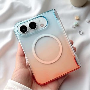 May include: A clear phone case with a blue to orange gradient finish, featuring a circular magnetic ring on the back. The case has a rectangular cutout for the camera lenses and flash, with a slim profile and a smooth, semi-transparent surface.