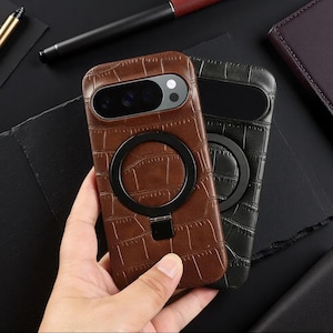 May include: Two smartphone cases with a brown and black crocodile-embossed texture. Each case features a prominent black circular magnetic ring stand on the back, designed for secure attachment and support, with a cutout for the camera module.