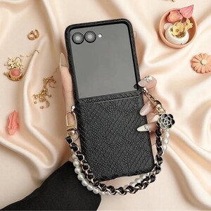 May include: A black foldable smartphone case with a textured snakeskin pattern. The case features a detachable wrist strap made of white faux pearls interwoven with a black leather-like cord, accented by a black and silver flower-shaped charm.