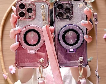 May include: Two glittery smartphone cases with metallic frames and integrated circular ring stands. The left case is rose gold, and the right case is purple. Both feature detachable matching fabric lanyards with gold-toned metal clips.