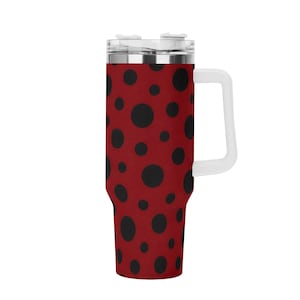 Puede incluir: Un vaso cilíndrico alto de acero inoxidable con un color base rojo vibrante adornado con un patrón repetitivo de puntos negros sólidos de varios tamaños. El recipiente incluye un asa blanca y una tapa de plástico transparente extraíble.