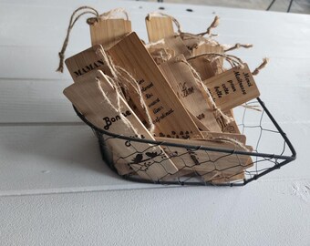 May include: A collection of rectangular bamboo bookmarks with jute twine loops, each featuring black printed French text and decorative motifs. The bookmarks are contained within a black wire mesh basket, showcasing natural wood grain textures.