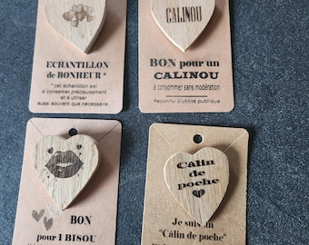 May include: Four light-colored wooden heart-shaped tokens attached to individual rectangular kraft paper cards. Each card features black printed text and graphics, including phrases like ECHANTILLON de BONHEUR, CALINOU, BON pour 1 BISOU, and Câlin de poche.