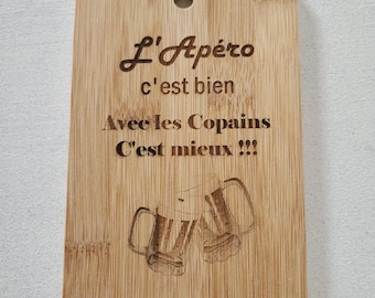 May include: A rectangular bamboo serving board with a hole at the top for hanging. The board features laser-engraved text that reads L'Apéro c'est bien Avec les Copains C'est mieux !!! and a graphic illustration of two clinking beer mugs.