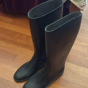 Puede incluir: Un par de botas altas de goma negra con un acabado mate liso y un diseño de punta redondeada. Estas botas hasta la rodilla presentan un exterior sencillo y sin adornos en color negro sólido, con una suela plana y una abertura ancha arriba.