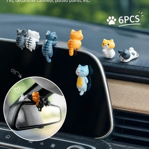 May include: A set of 6PCS Cute Cat Decorations featuring small, colourful cat figurines in various poses. The cats are depicted in grey, white, blue, orange, and black-and-white patterns, designed to hang on edges like car screens or monitors.