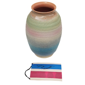 May include: A ceramic vase with a textured, cross-hatched surface featuring a gradient of green, pink, and blue hues, topped with a smooth terracotta rim. Below the vase is a rectangular tag with a blue stripe and the text Dan and Marcelle.