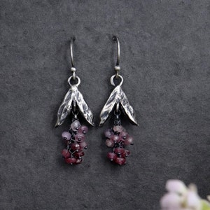 May include: Silver earrings with a cluster of pink and purple gemstones hanging from a leaf-shaped design.