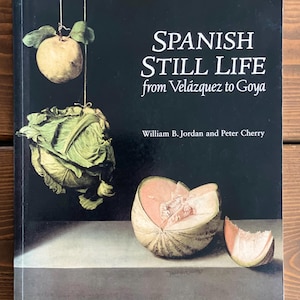 May include: A hardback book titled Spanish Still Life from Velázquez to Goya by William B. Jordan and Peter Cherry. The black cover features a painting of a hanging quince, a cabbage, and a sliced melon on a ledge against a dark background.