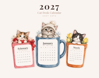 Op de afbeelding: Een 2027 kattenbureaukalender met 12 uitgesneden kaarten in A4 en US Letter formaat. De afbeelding toont februari, januari en maart met illustraties van kittens in een roze doos, een blauwe mok en een oranje pot met tulpen.