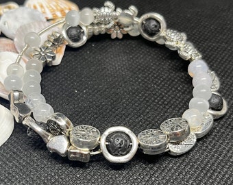 Memory wire bracelet with white  jade, black lava beads, tree of life, turtle, heart and flower beads, and silver bead-holding spacers.