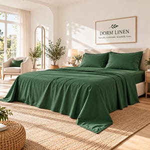 May include: A bed set featuring a solid dark green flat sheet and two matching pillowcases. The bedding is draped over a mattress on a bed frame. A framed sign above the bed displays the text DORM LINEN Naturally Comfortable, Beautifully Yours.