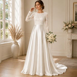 Può includere: Un abito da sposa bianco lungo fino a terra con corpetto in pizzo a maniche lunghe, scollo rotondo e gonna in raso liscio e fluido. L'abito presenta un punto vita aderente che si apre in un orlo ampio che sfiora il pavimento con uno strascico.