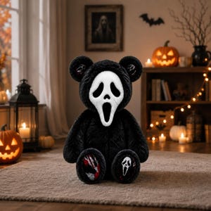 Könnte beinhalten: Ein Plüschteddybär mit schwarzem Fell, der eine weiße Ghostface-Maske trägt. Der Bär hat schwarze Ohren mit kleinen weißen Maskensymbolen, und die Fußsohlen zeigen einen blutigen rot-weißen Handabdruck sowie eine weiße Ghostface-Maske.