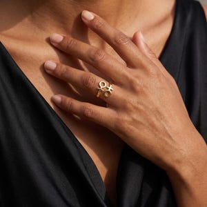 May include: A gold-toned ring featuring two distinct symbols: a circle with a downward cross representing the female gender sign and a circle with an upward cross representing the male gender sign, connected by a thin, polished metal band.