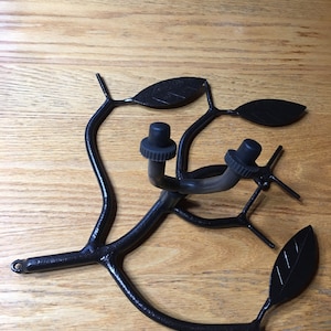 Könnte beinhalten: Schwarzer Gitarrenständer aus Metall in Form eines Astes mit Blättern. Der Ständer hat zwei schwarze Knöpfe zum Festhalten der Gitarre.